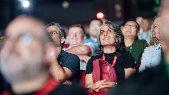 A woman listening to a conference in the middle of a seated crowd