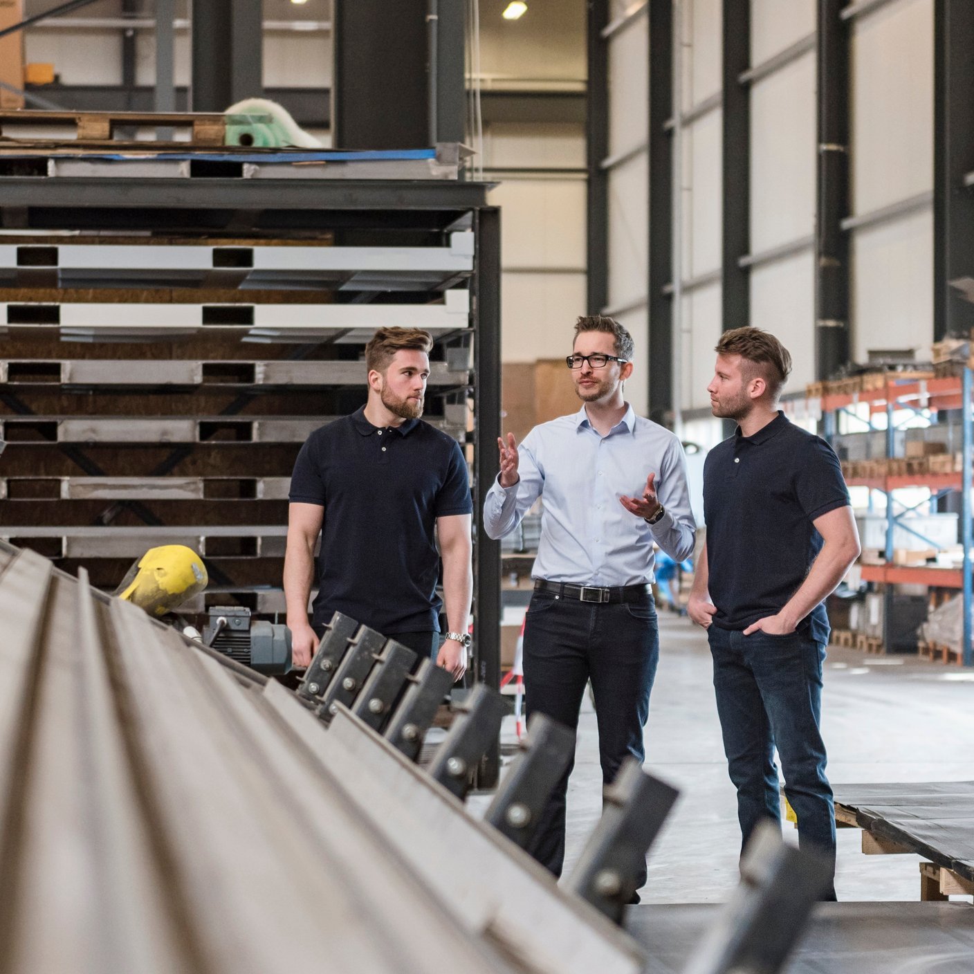 Three men talking on factory shop floor (cropped)