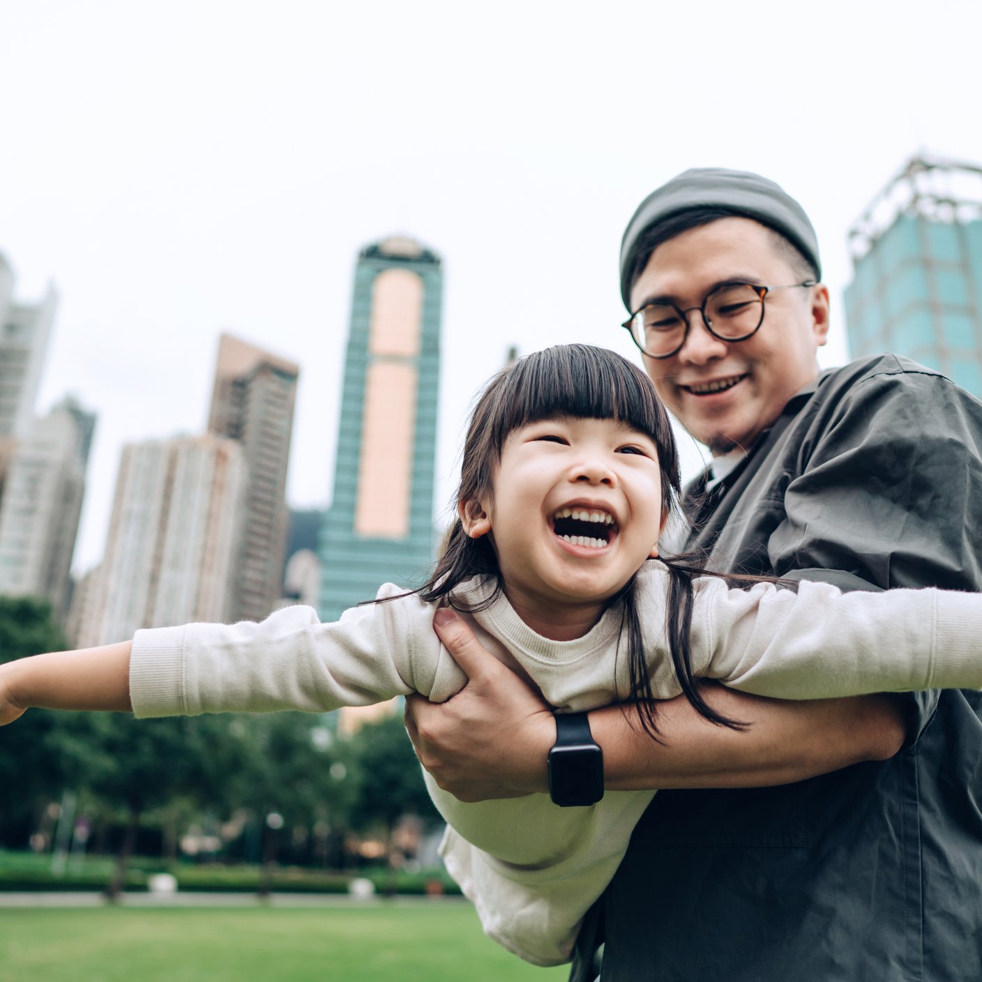 Happy little Asian girl having fun with her father outdoors in urban park.