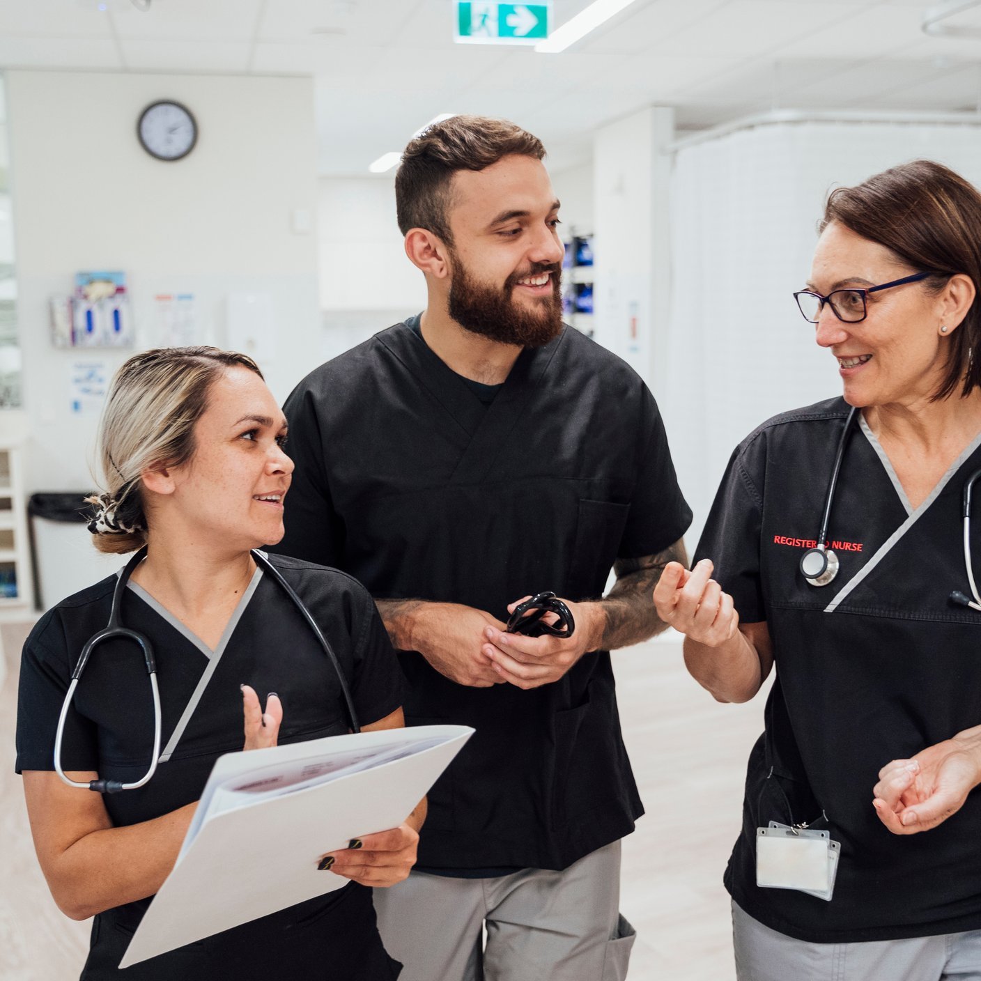 A shot of three healthcare workers walking and talking through the hospital ward.