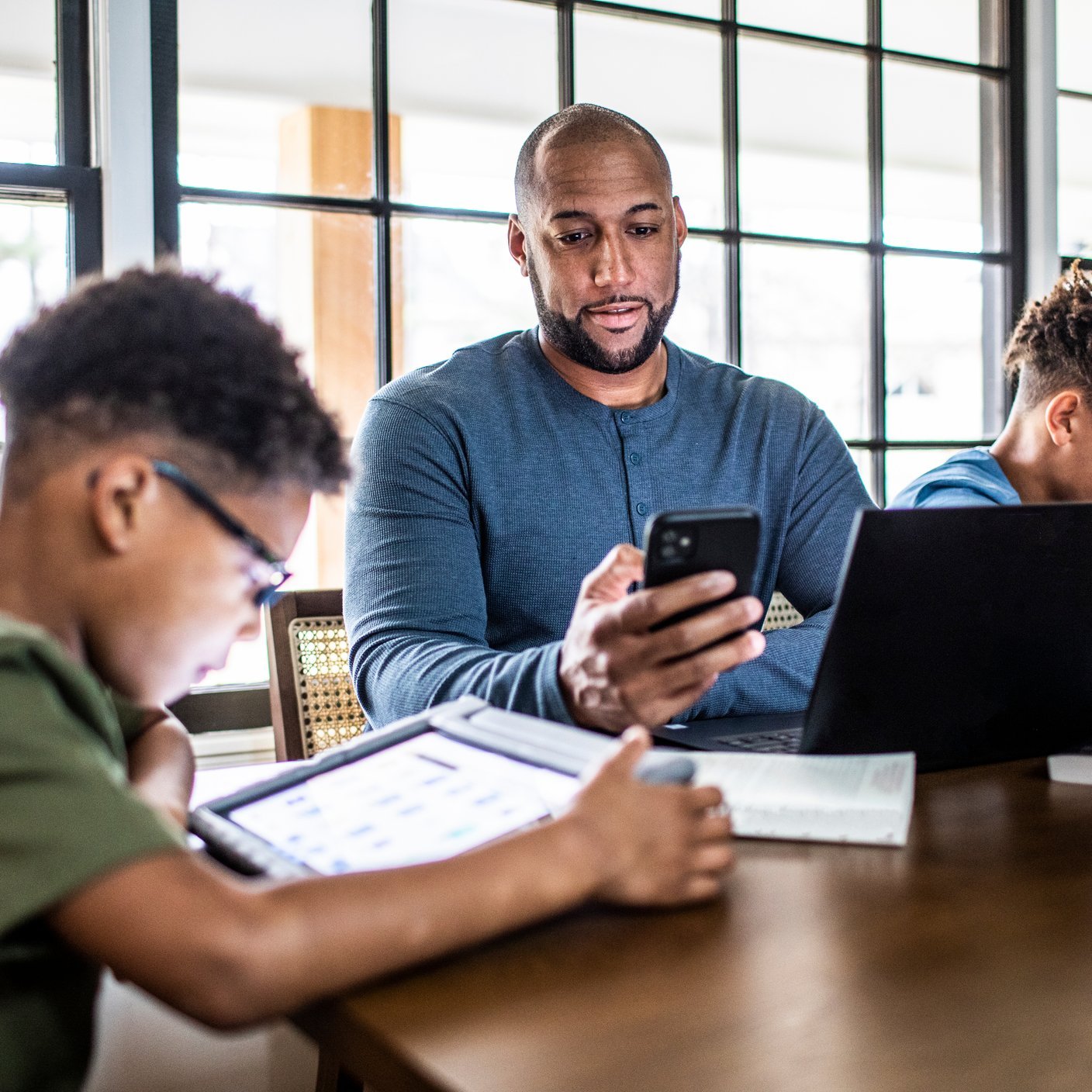 Father working from home in residential kitchen with family in background
