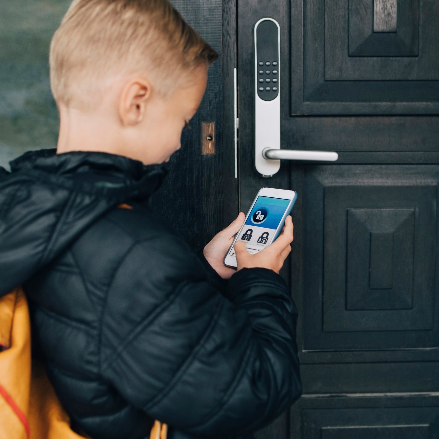 Rear view of boy using app on smart phone to unlock house door