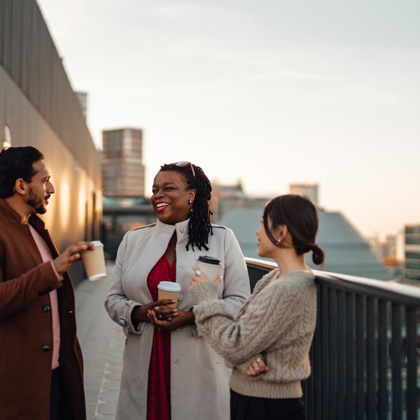 Cheerful multi-ethnic business people standing by railing at rooftop
