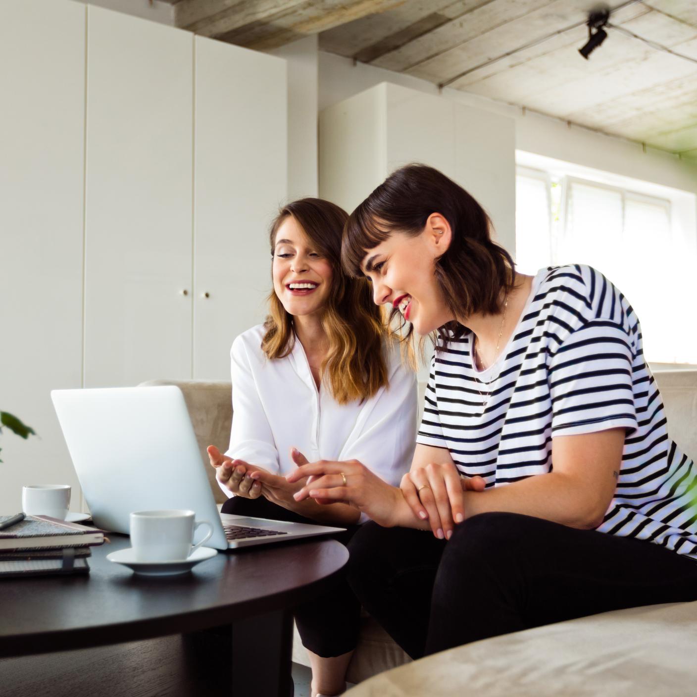 Young women sitting on sofa in the creative workplace and working together over laptop.