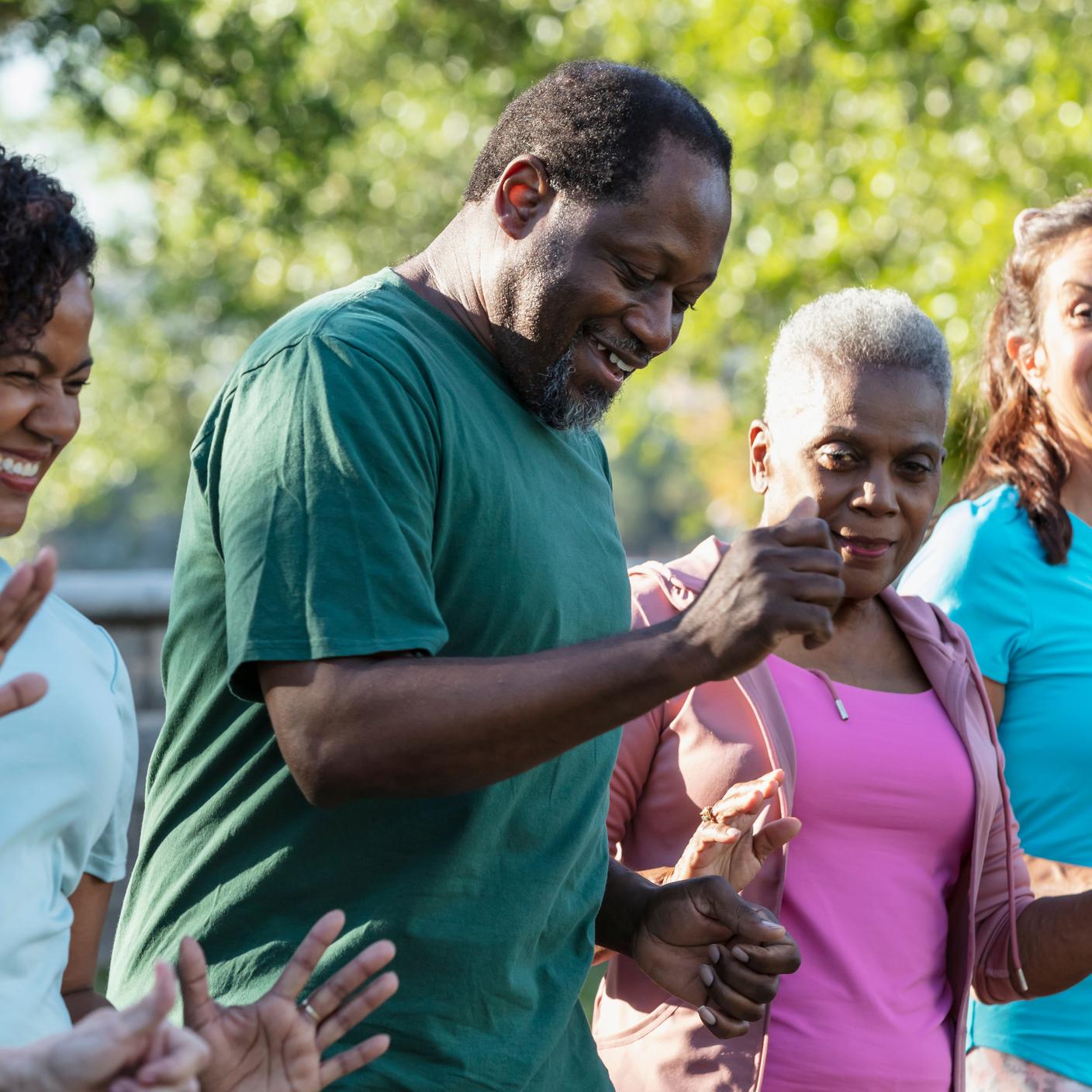 Un groupe de cinq adultes aux origines diverses participent à un cours de danse dans un parc.