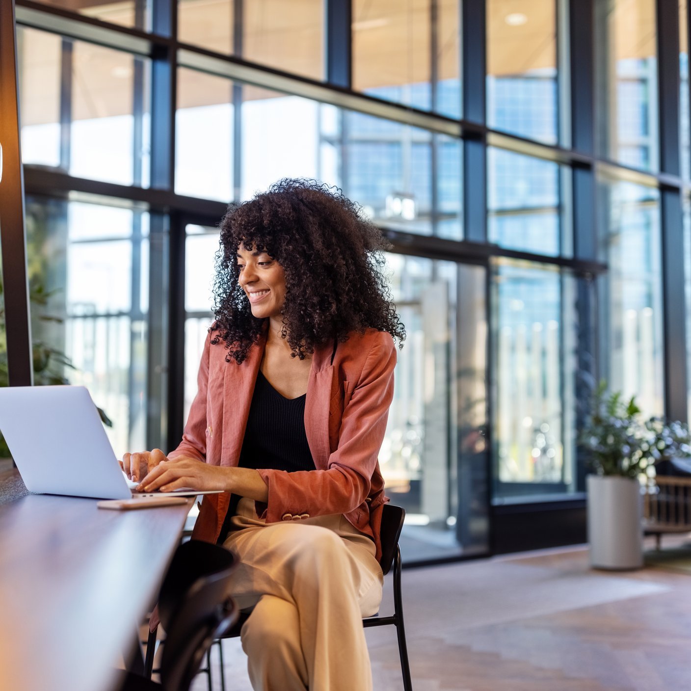Young African woman working on laptop at office cafe. Happy female entrepreneur sitting in office lobby using laptop.