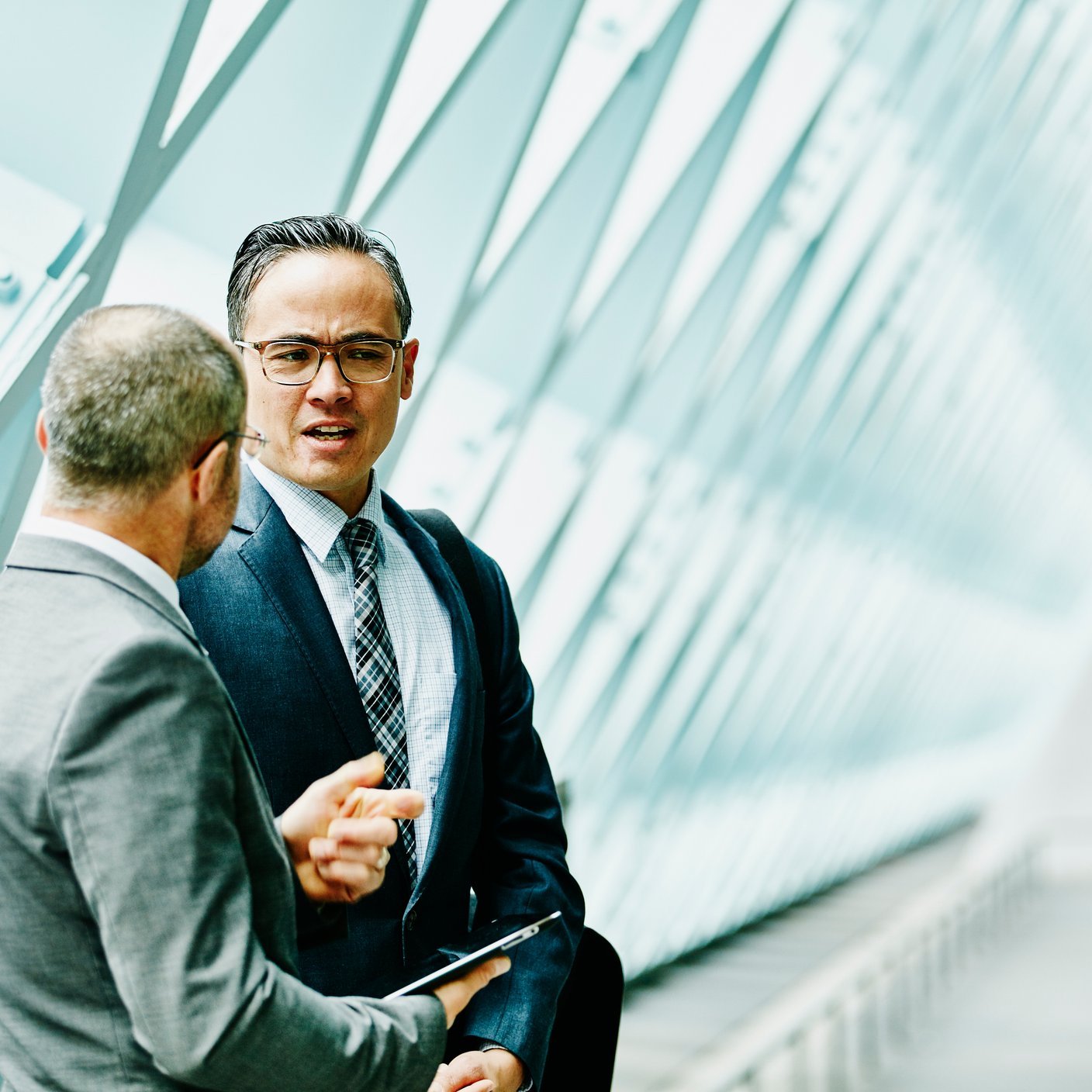 Two businessmen discussing data on digital tablet in informal meeting in building corridor