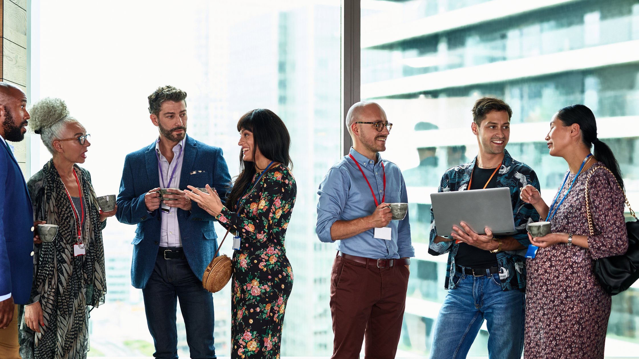 Business people chatting at corporate event, meeting in corporate bar by large window, young man using laptop.